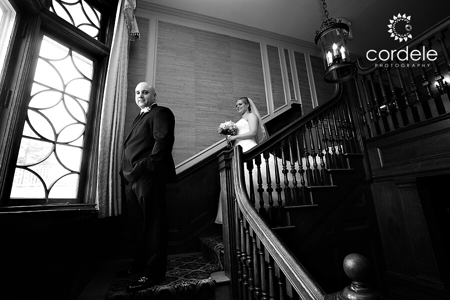 A groom looks at a camera while waiting for bride to walk down the stairs for his first glimpse at him.